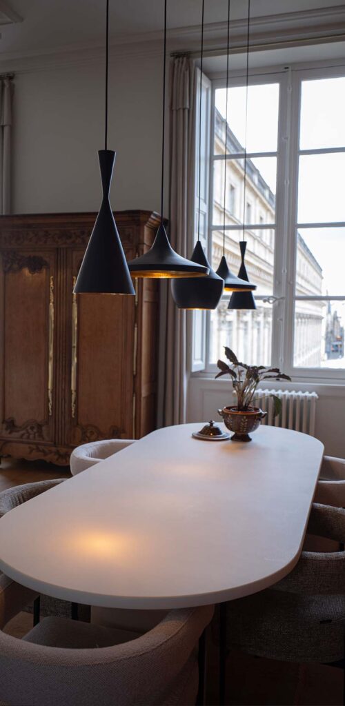 Suspensions noires en cascade au-dessus d'une table à manger, fenêtre à petits carreaux sur cour bordelaise