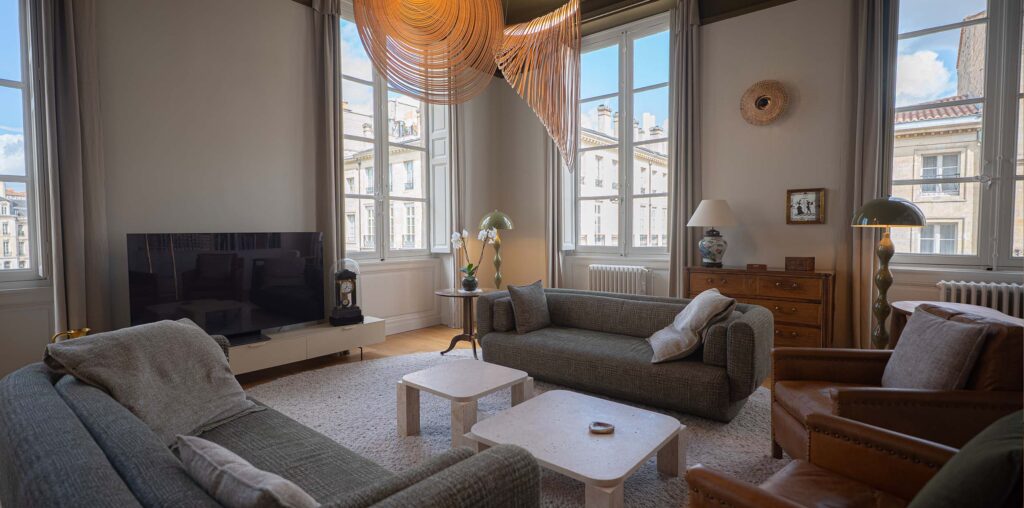 Salon avec fauteuil en cuir et suspension en rotin, vue sur les immeubles en pierre de Bordeaux