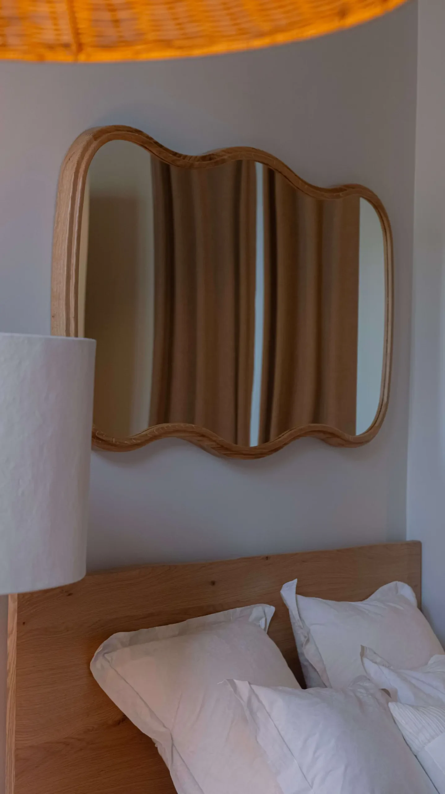 Miroir ondulé à cadre en chêne au-dessus d'une tête de lit en bois, suspension en rotin